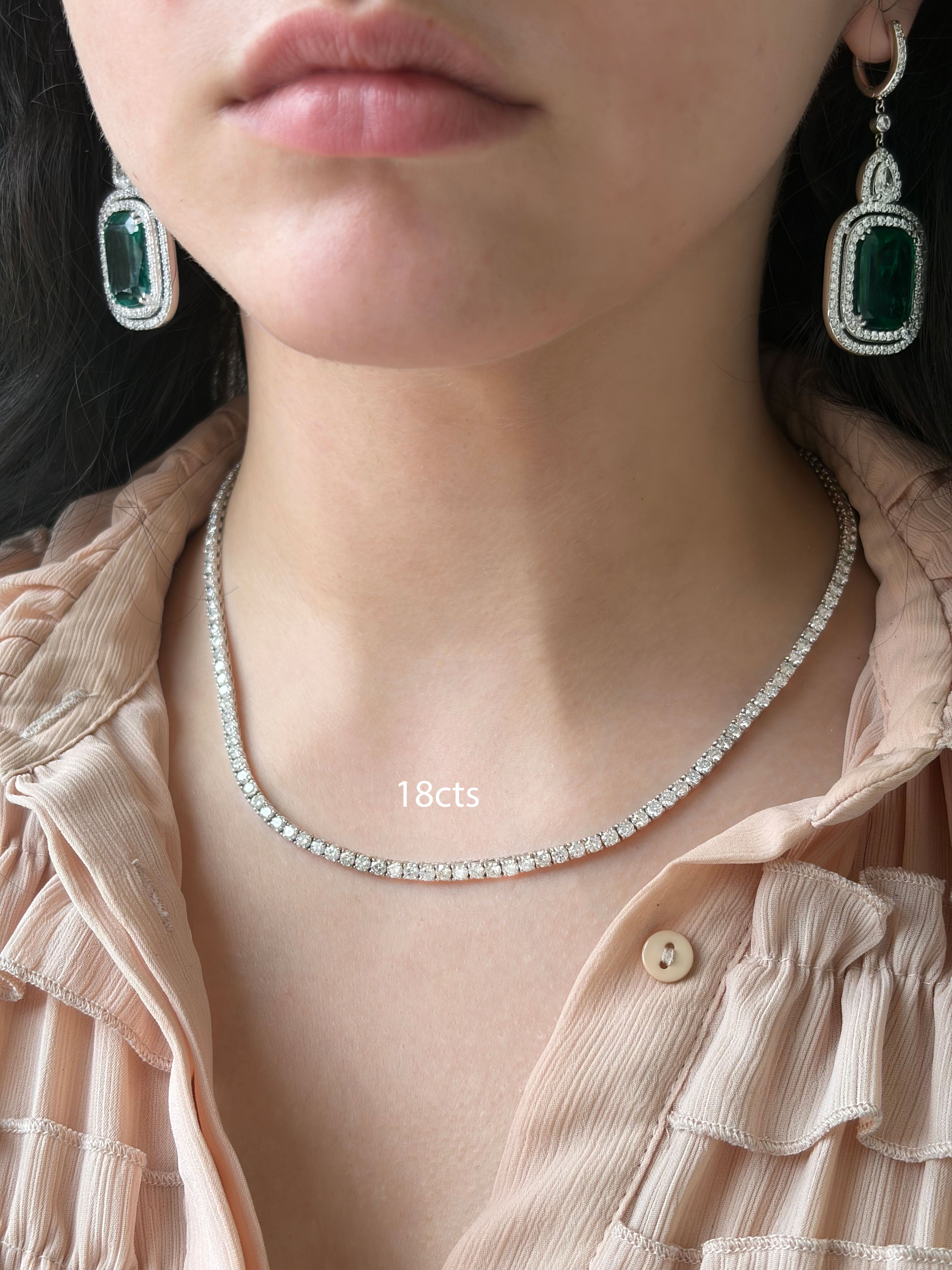 Close-up of a person wearing a diamond necklace and emerald earrings.