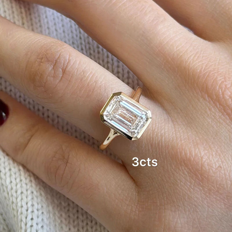 Bezel-set emerald cut lab-grown diamond solitaire ring in 18k yellow gold on hand