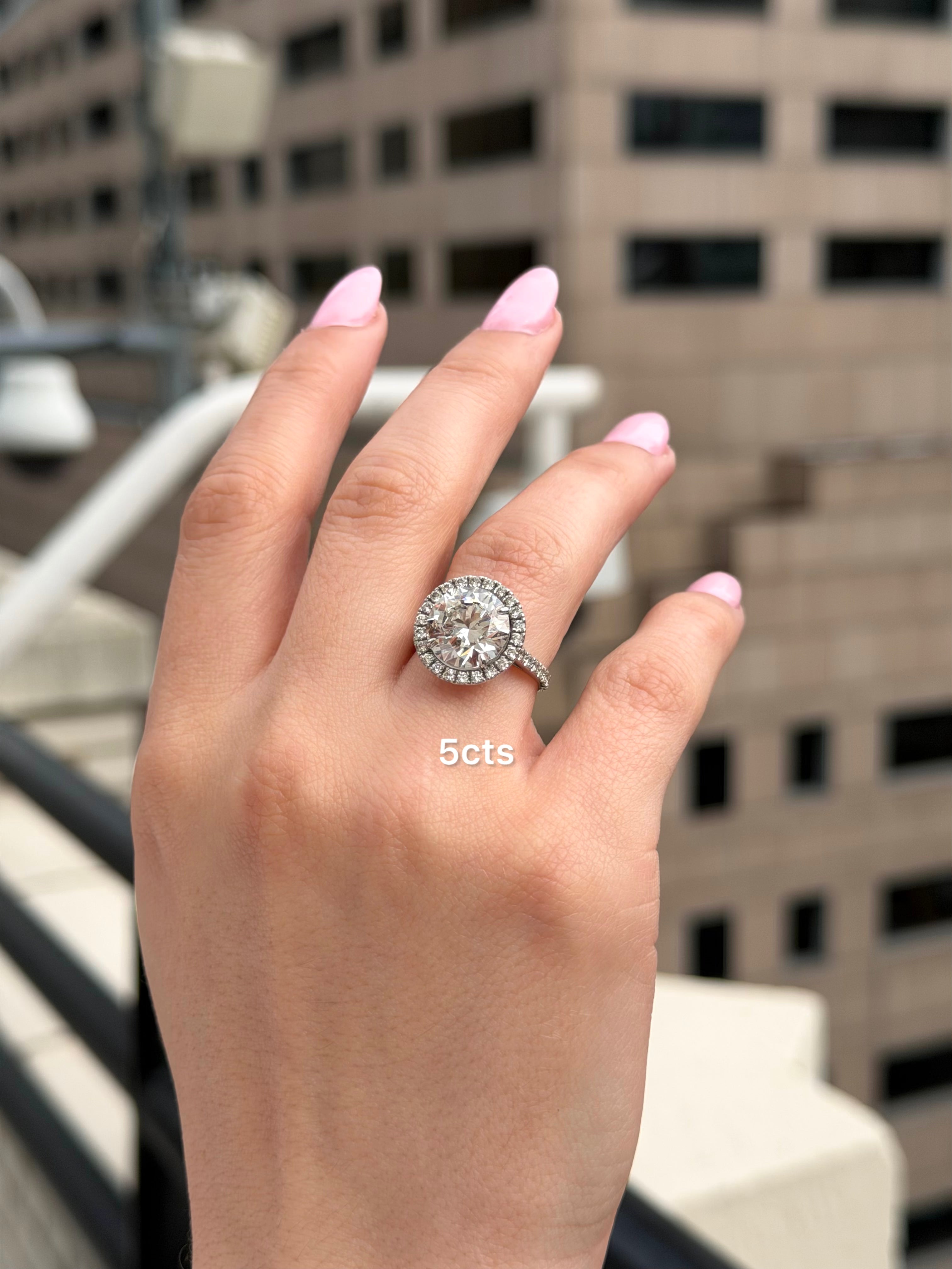 Hand wearing a diamond ring with '5 cts' text against a blurred urban background