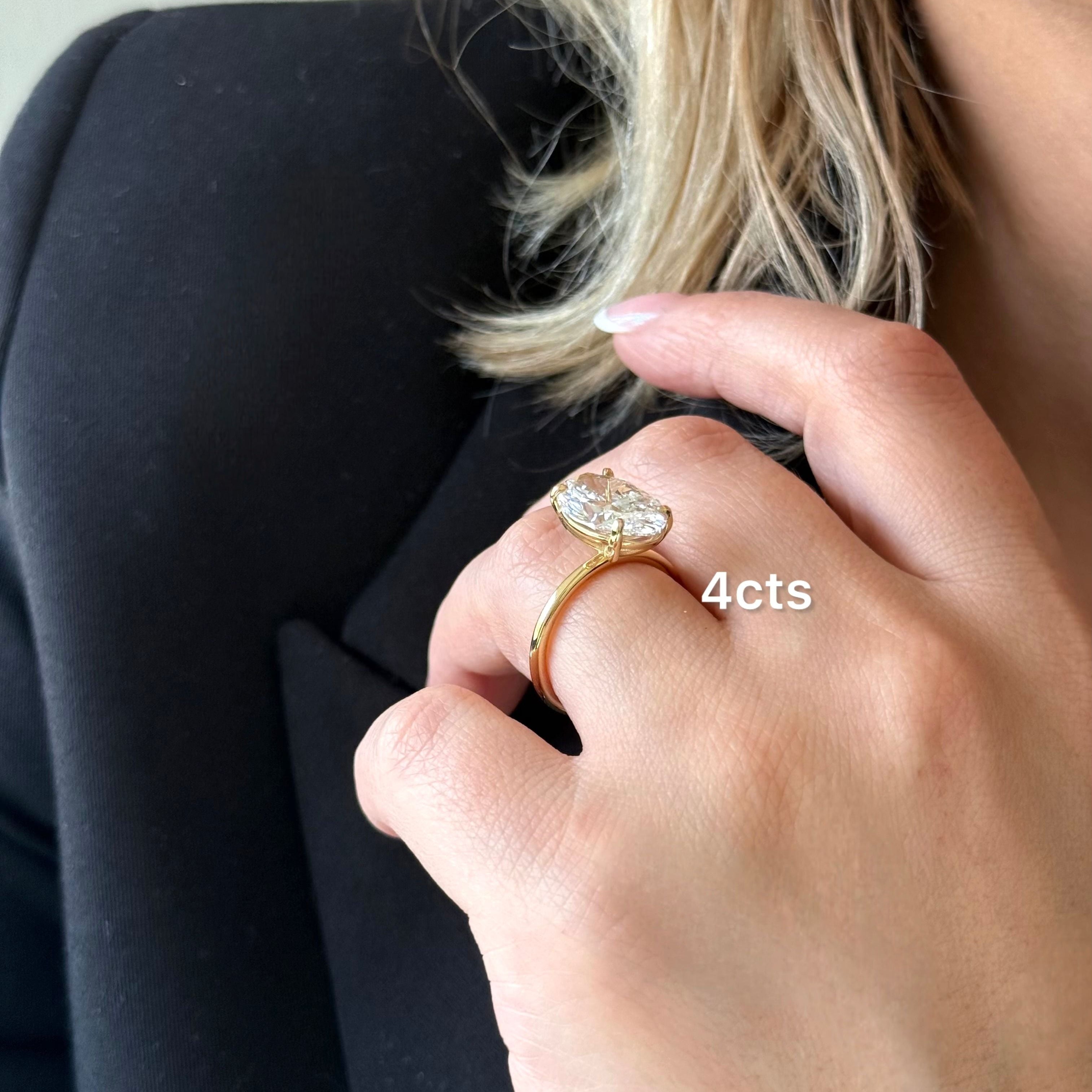 Close-up of a hand wearing a gold ring with a diamond, labeled '4cts', against a neutral background.