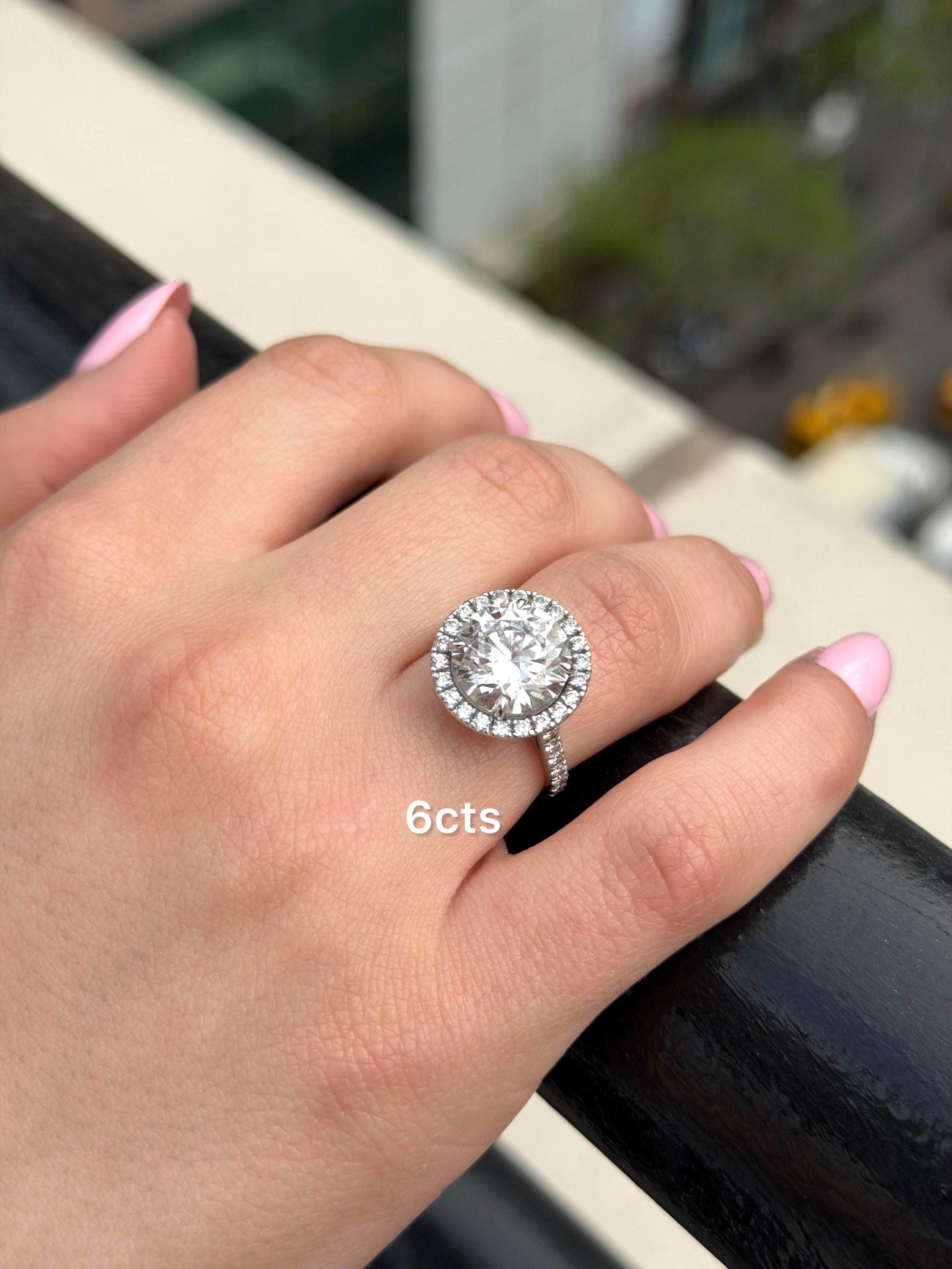 Hand wearing a diamond ring with '6cts' text, blurred background