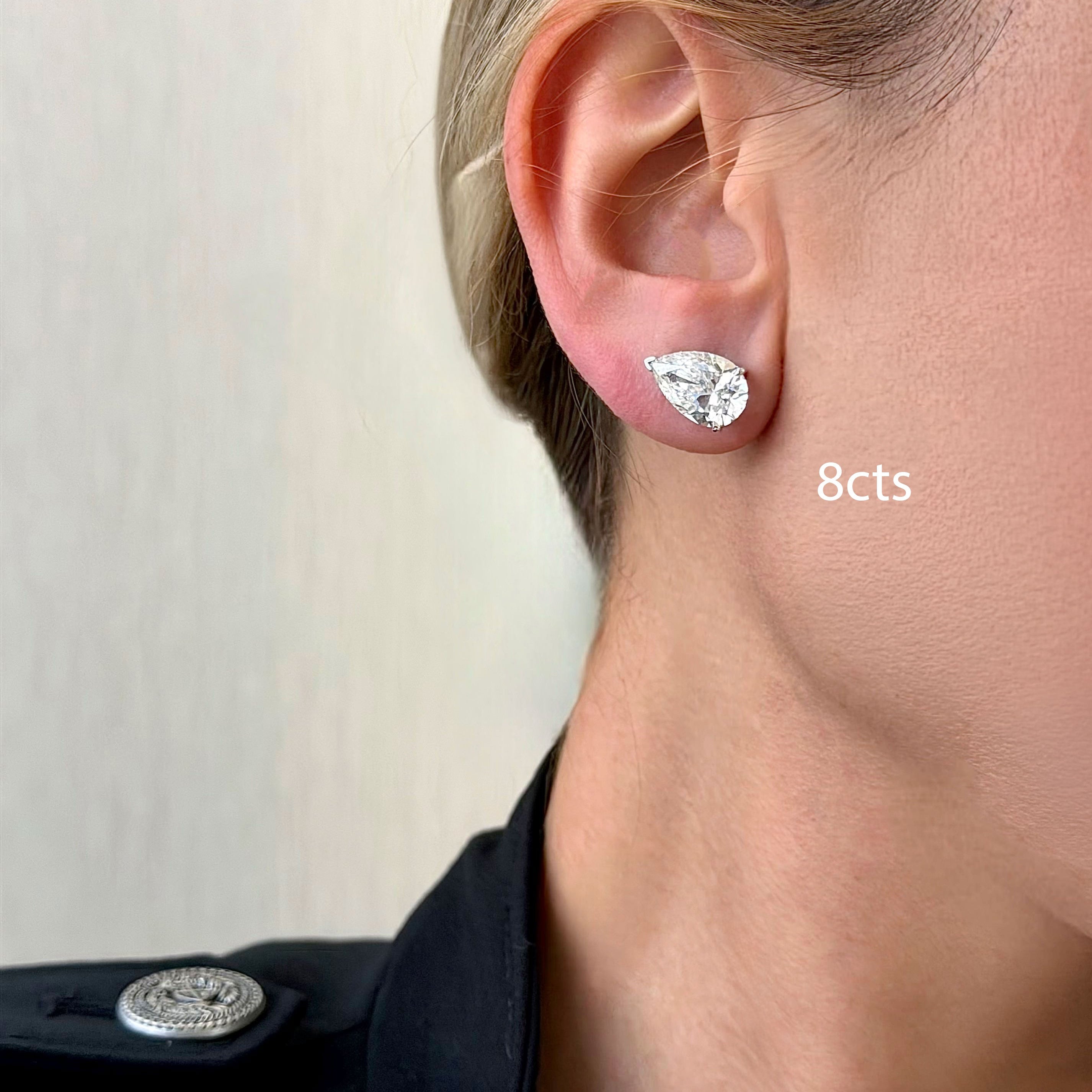 Close-up of a person wearing a diamond earring with '8cts' text on a neutral background