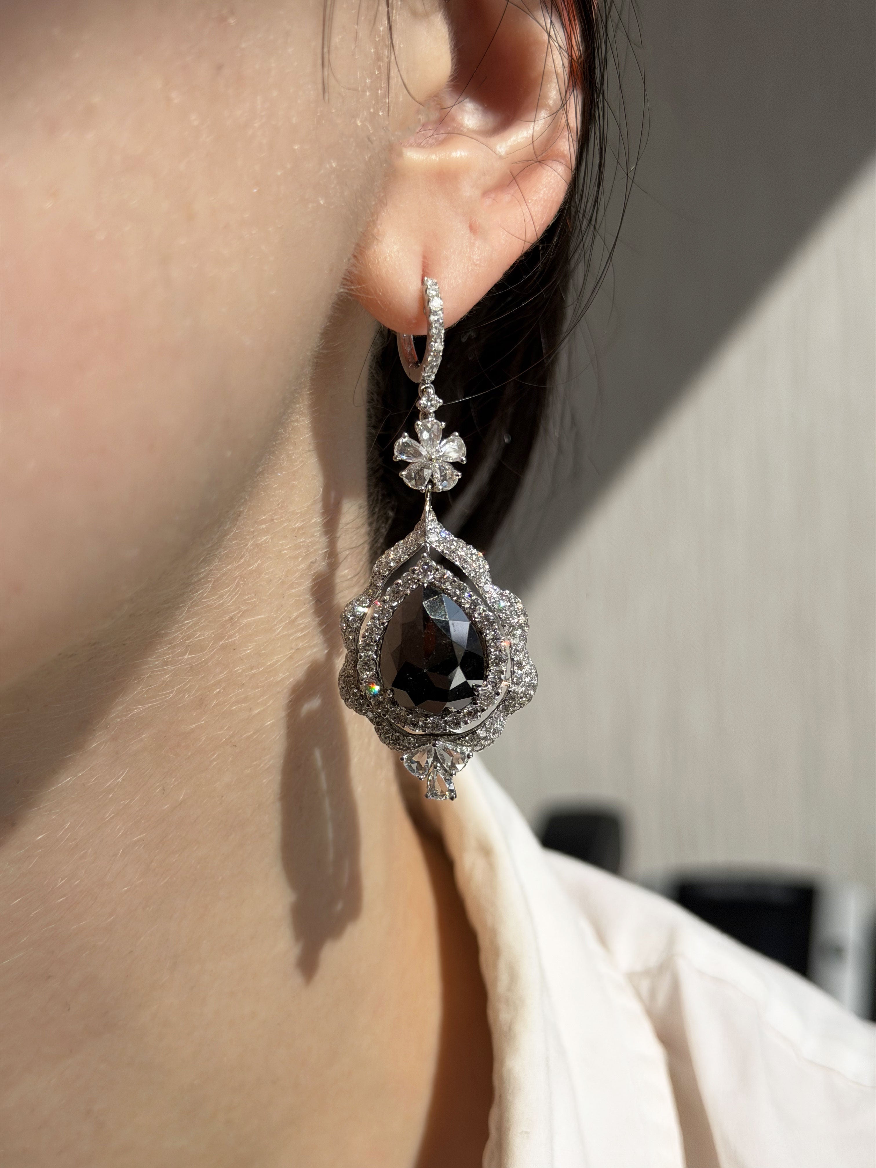 Close-up of a person wearing a black teardrop earring with silver detailing.