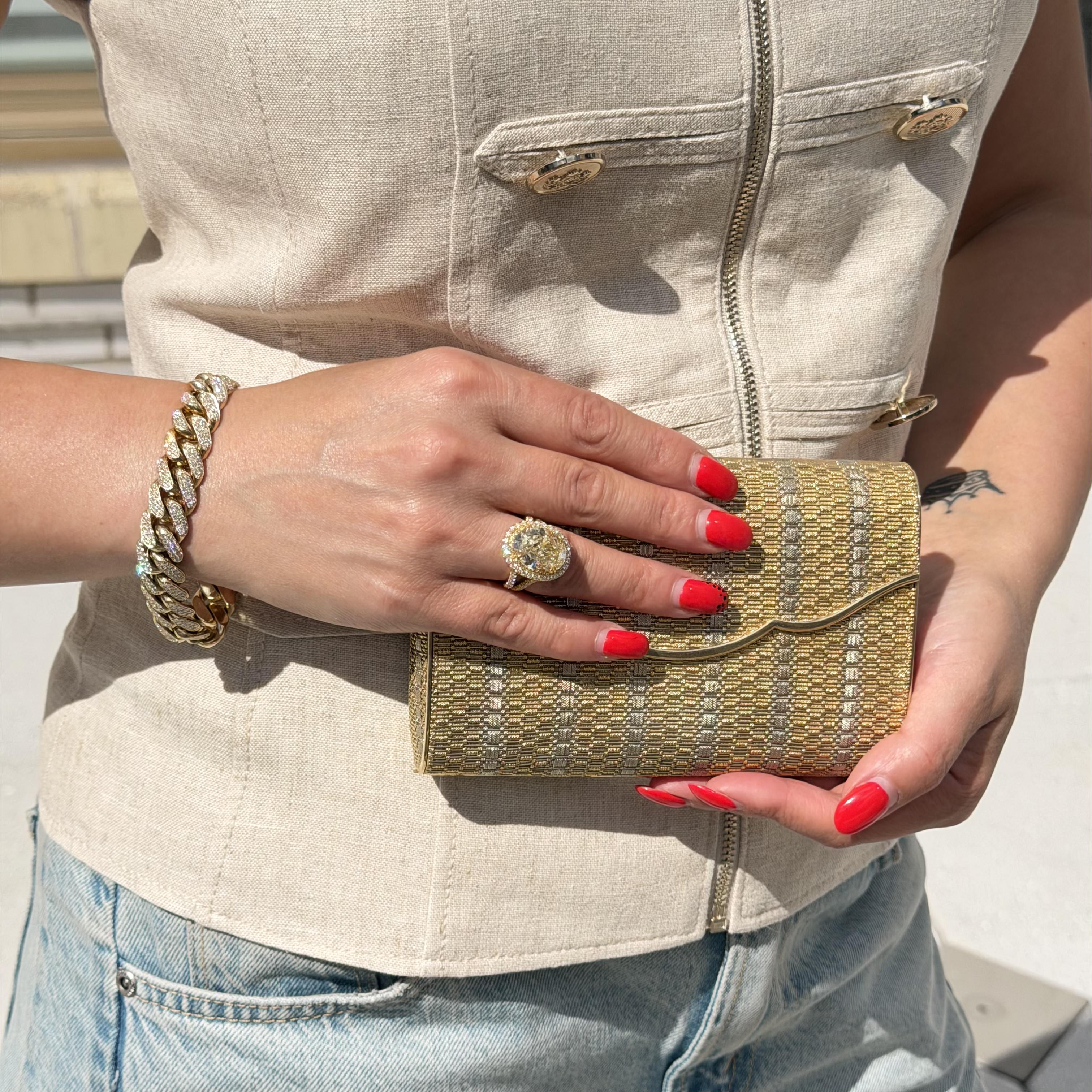 Person holding a gold clutch with red nail polish and a gold ring.