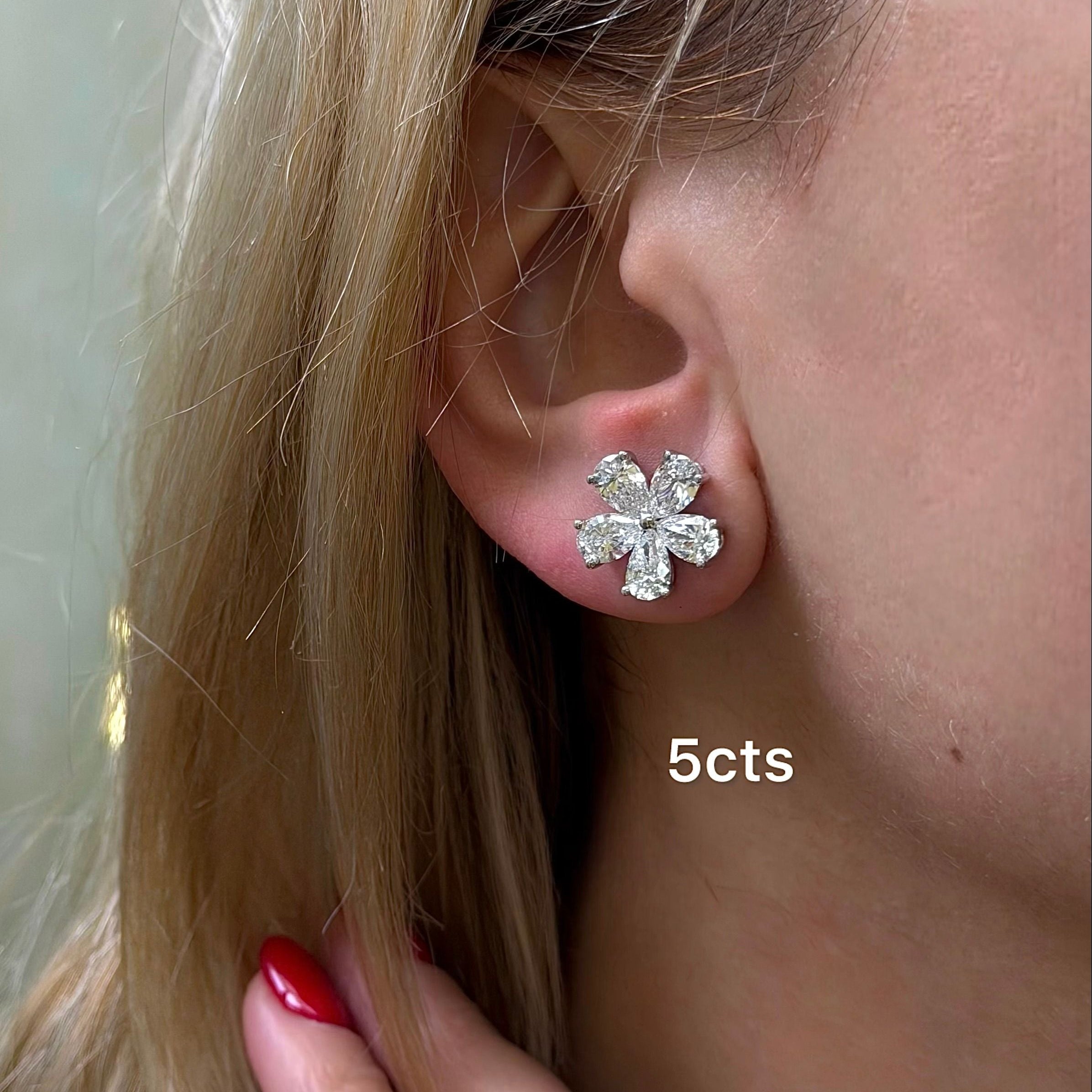 Close-up of a person wearing a diamond flower earring with '5cts' label.