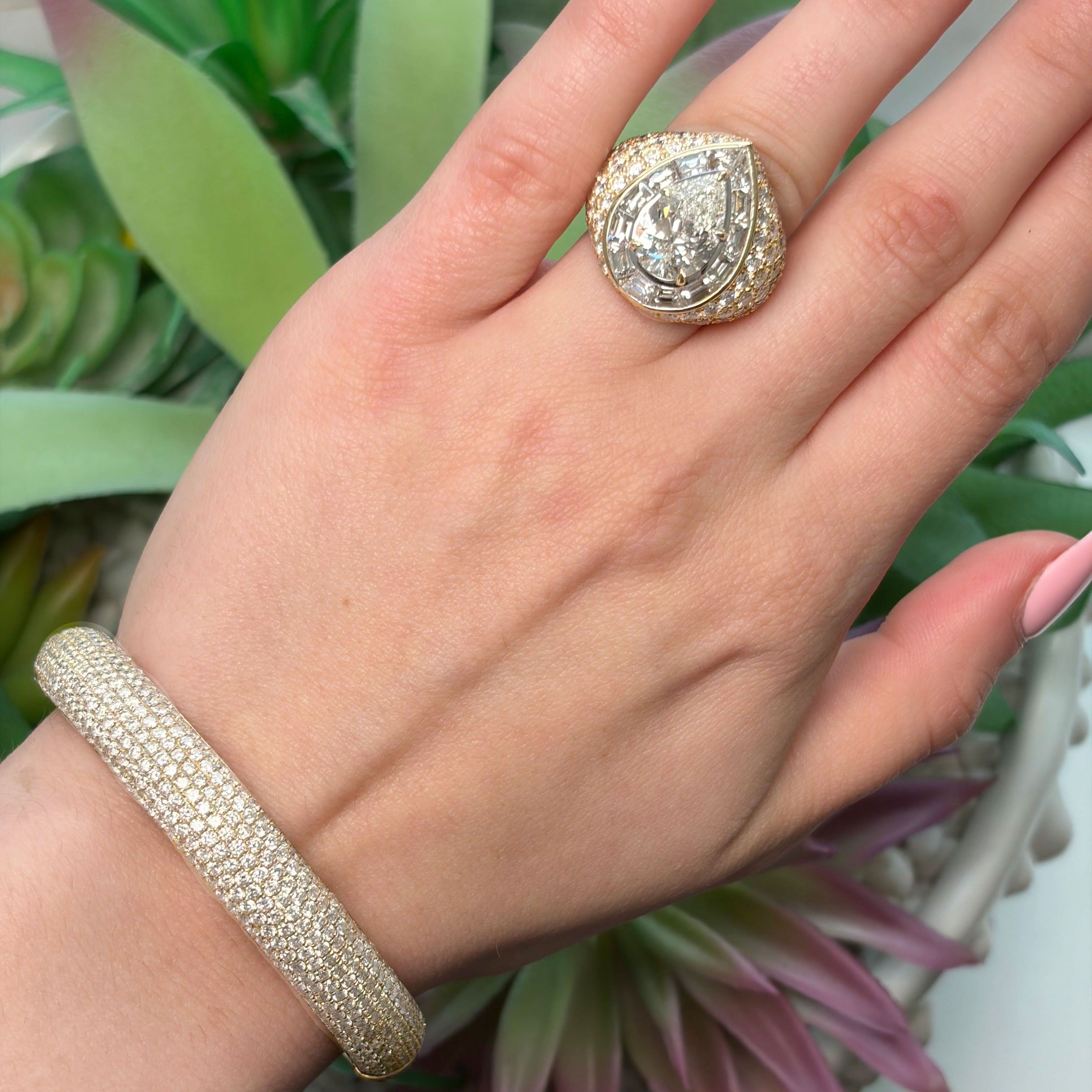 Hand wearing a gold ring and bracelet with a plant in the background