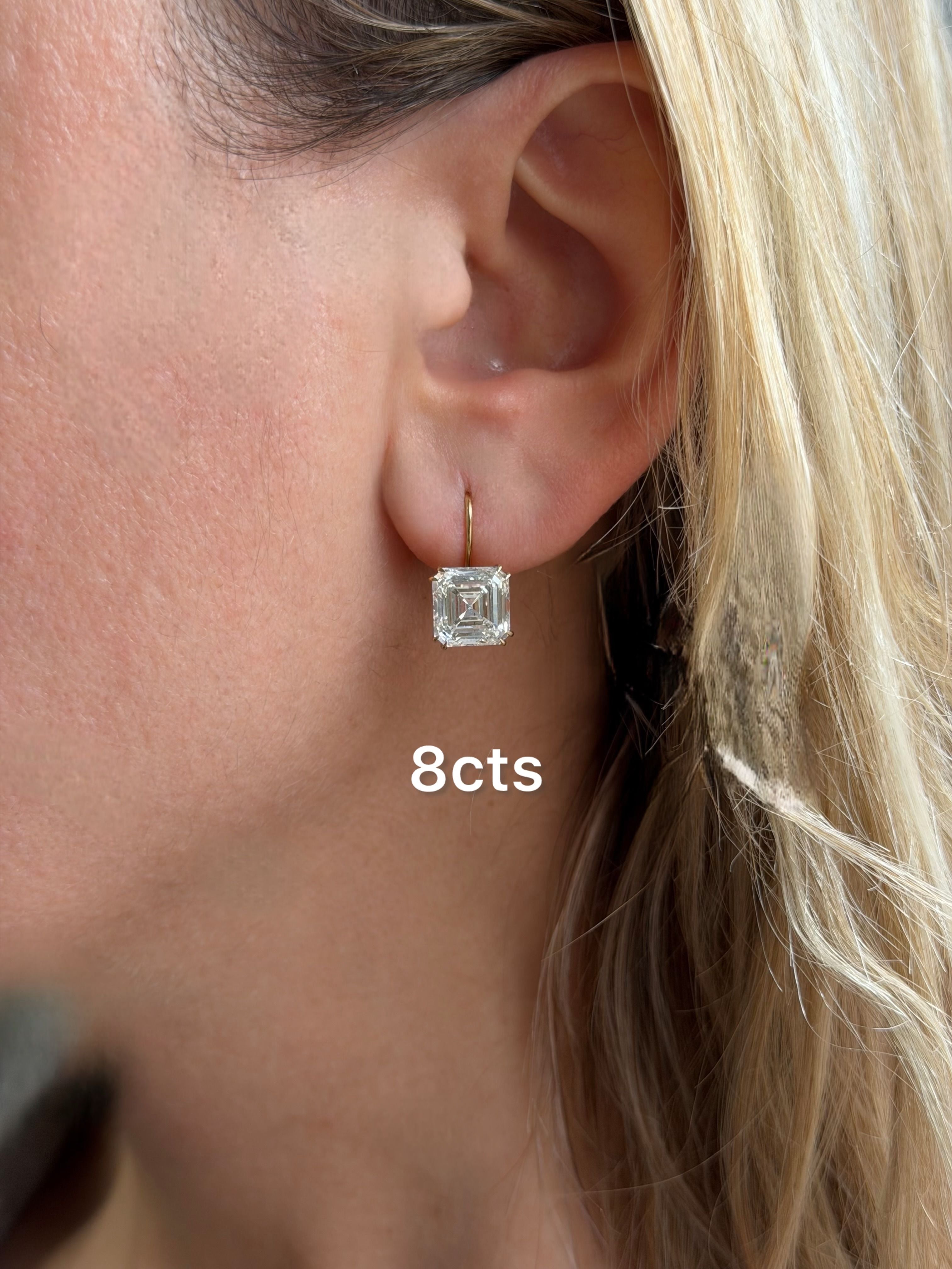 Close-up of an ear wearing a diamond earring with '8cts' text.