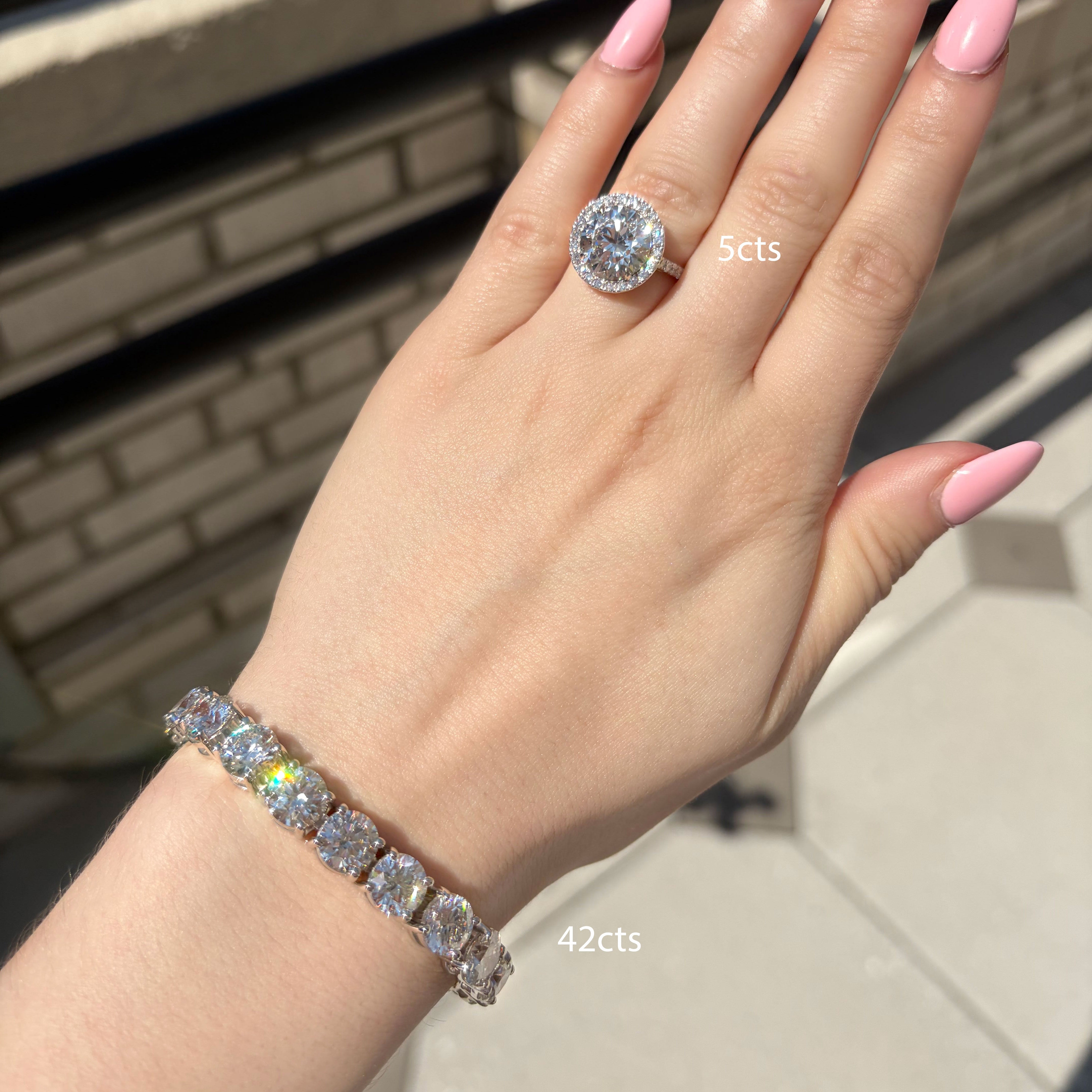 Hand wearing a diamond ring and bracelet with '42cts' text, outdoor background
