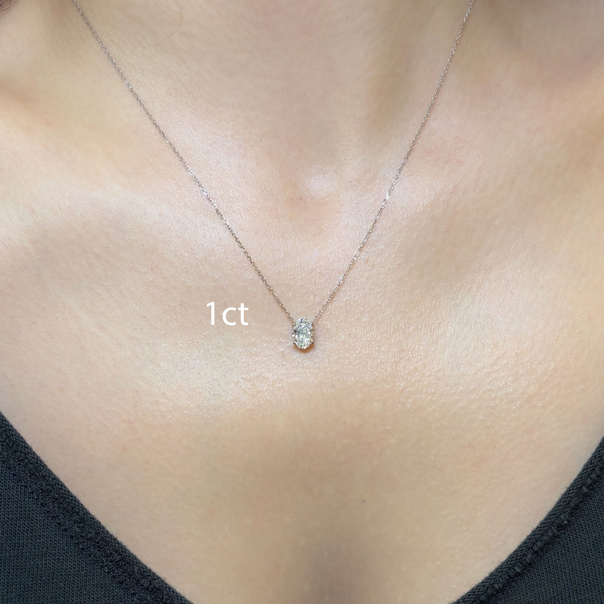 A close-up of a delicate silver chain necklace with a small teardrop-shaped clear gemstone pendant, worn on a model's neck. The text '1ct' is overlaid near the center.