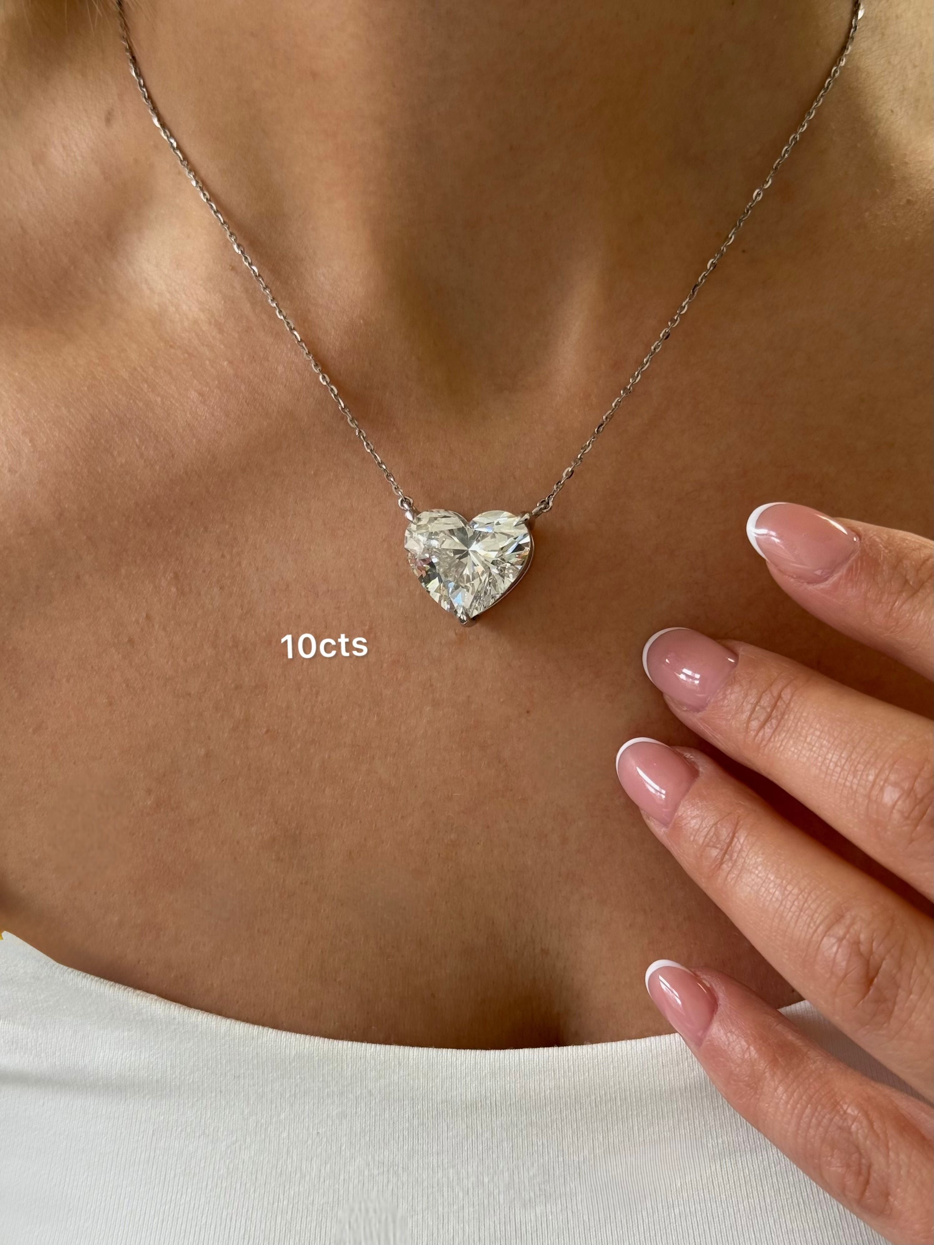 Heart-shaped diamond necklace with '10 cts' on a person's neck