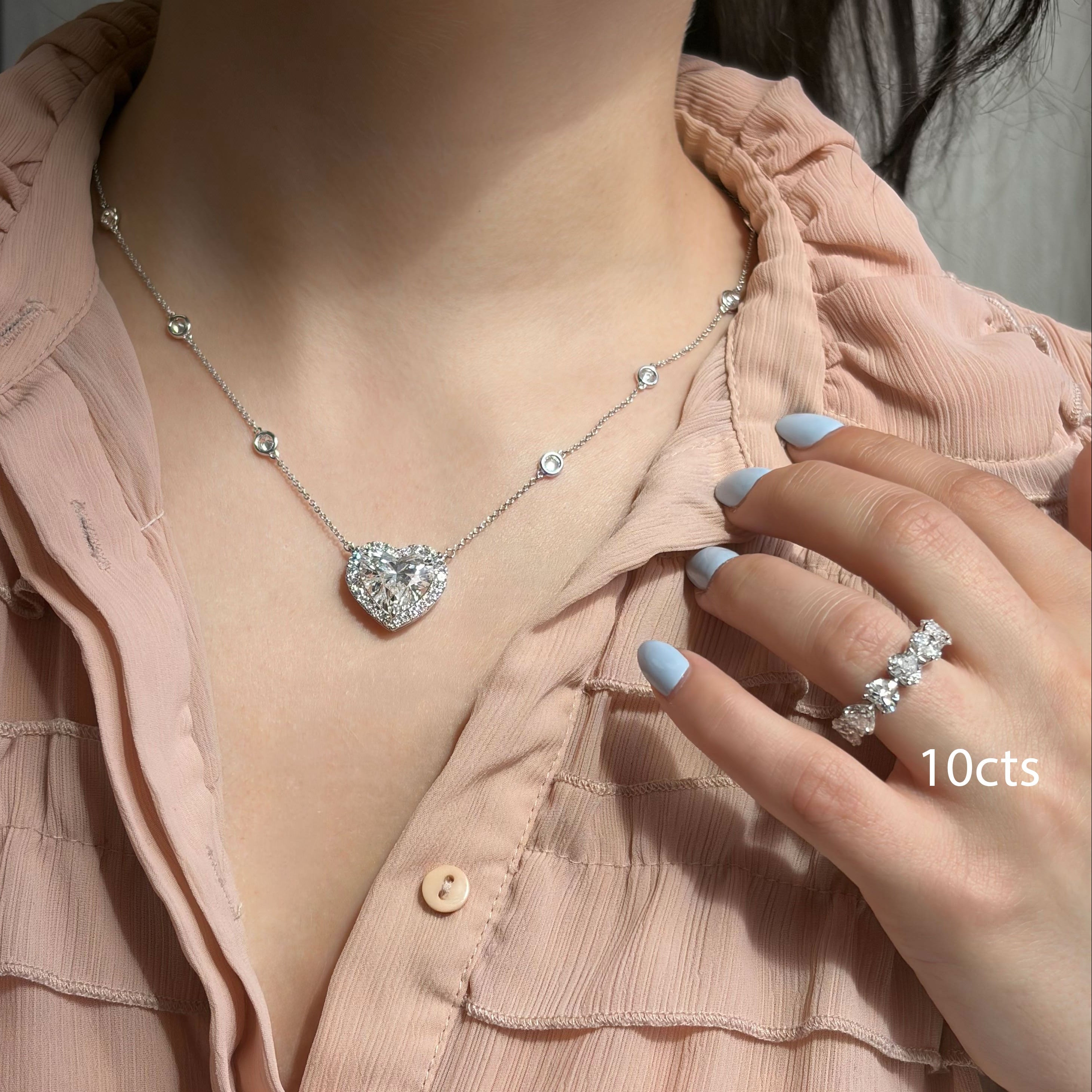 Person wearing a heart-shaped diamond necklace and ring with a soft pink shirt.