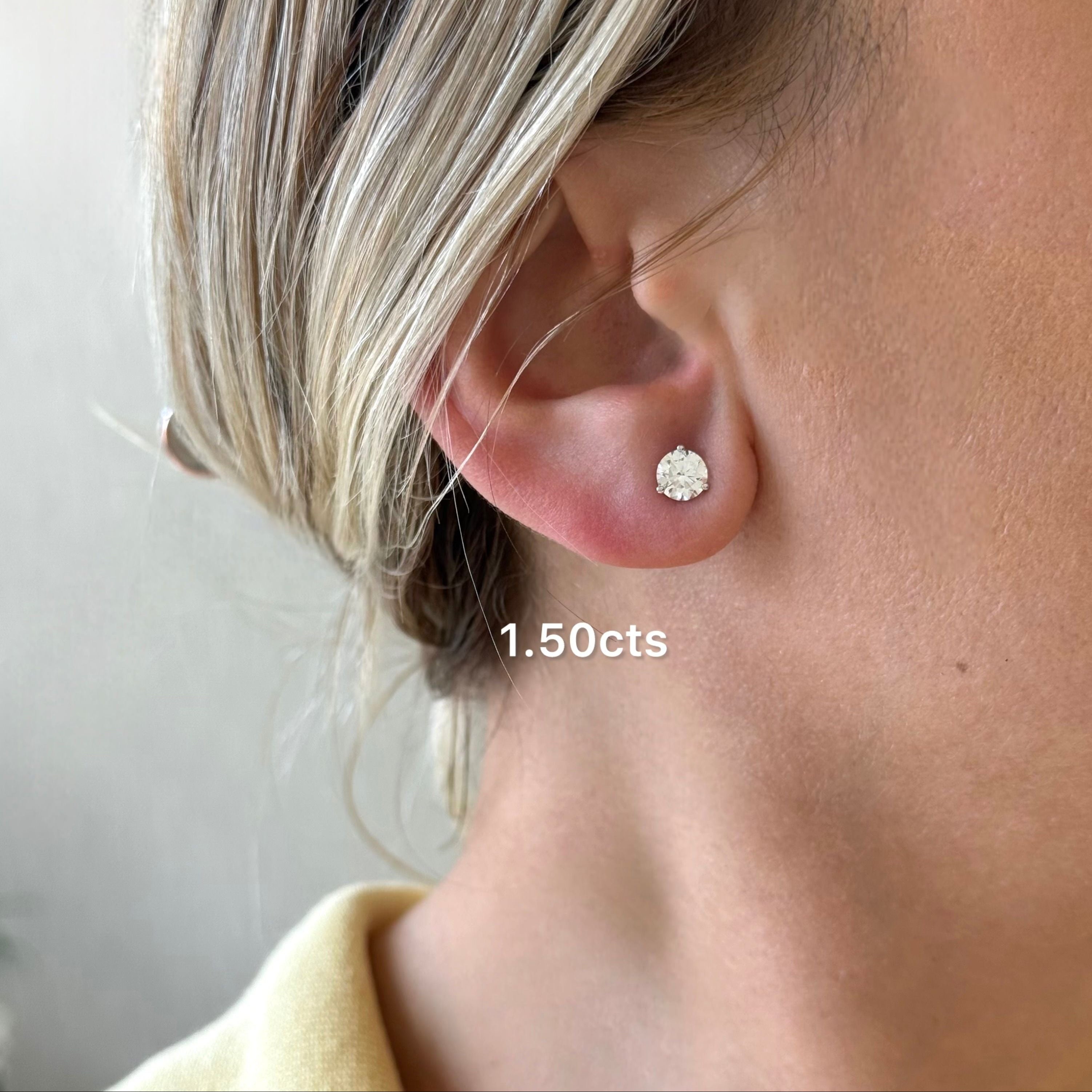 Close-up of an ear wearing a diamond stud earring with '1.50cts' text.