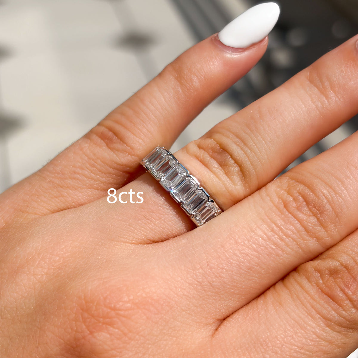A close-up of a hand wearing a silver band ring with eight baguette-cut clear stones. The text '8cts' is overlaid on the image, indicating the carat weight of the stones.