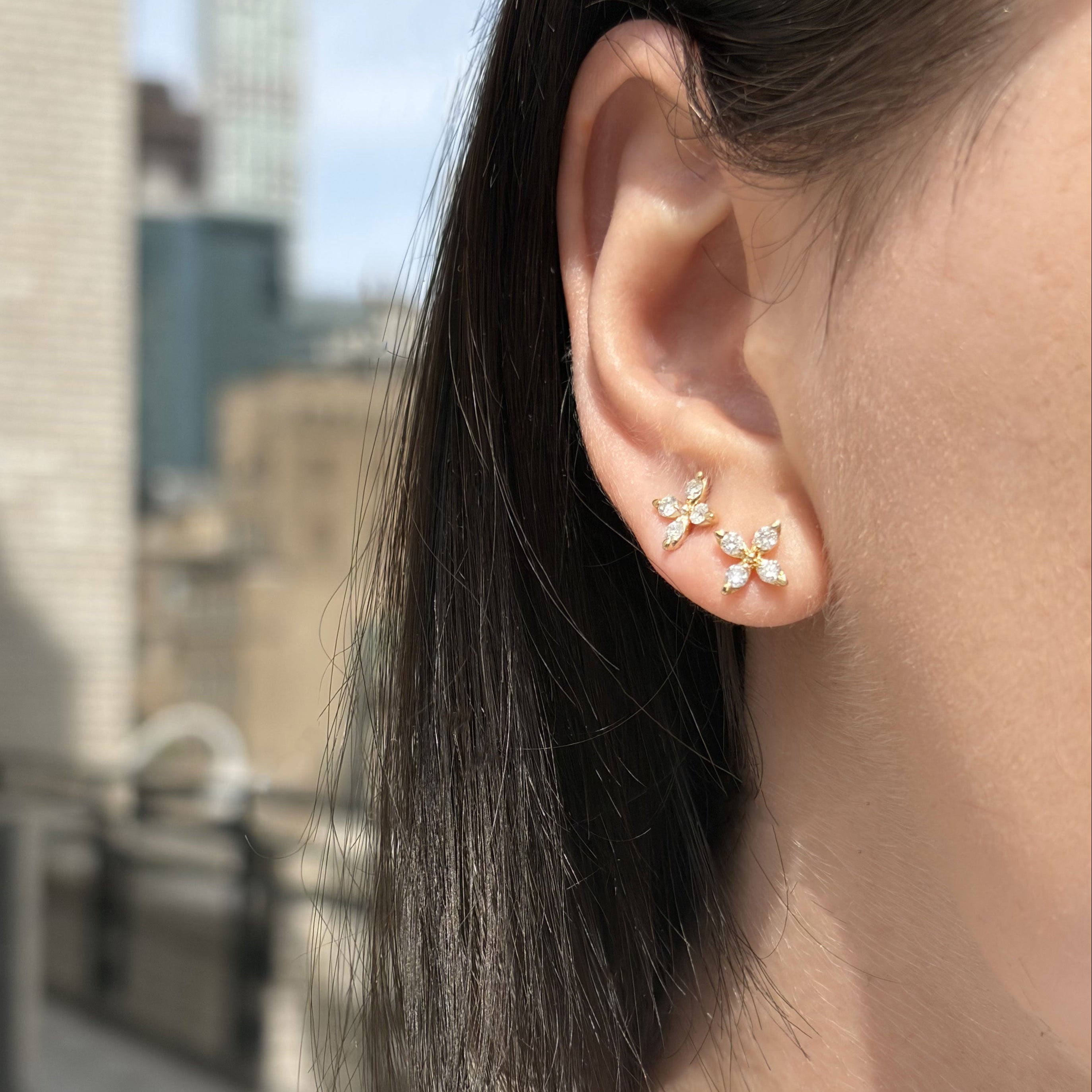 Close-up of an ear wearing a floral earring with a cityscape background