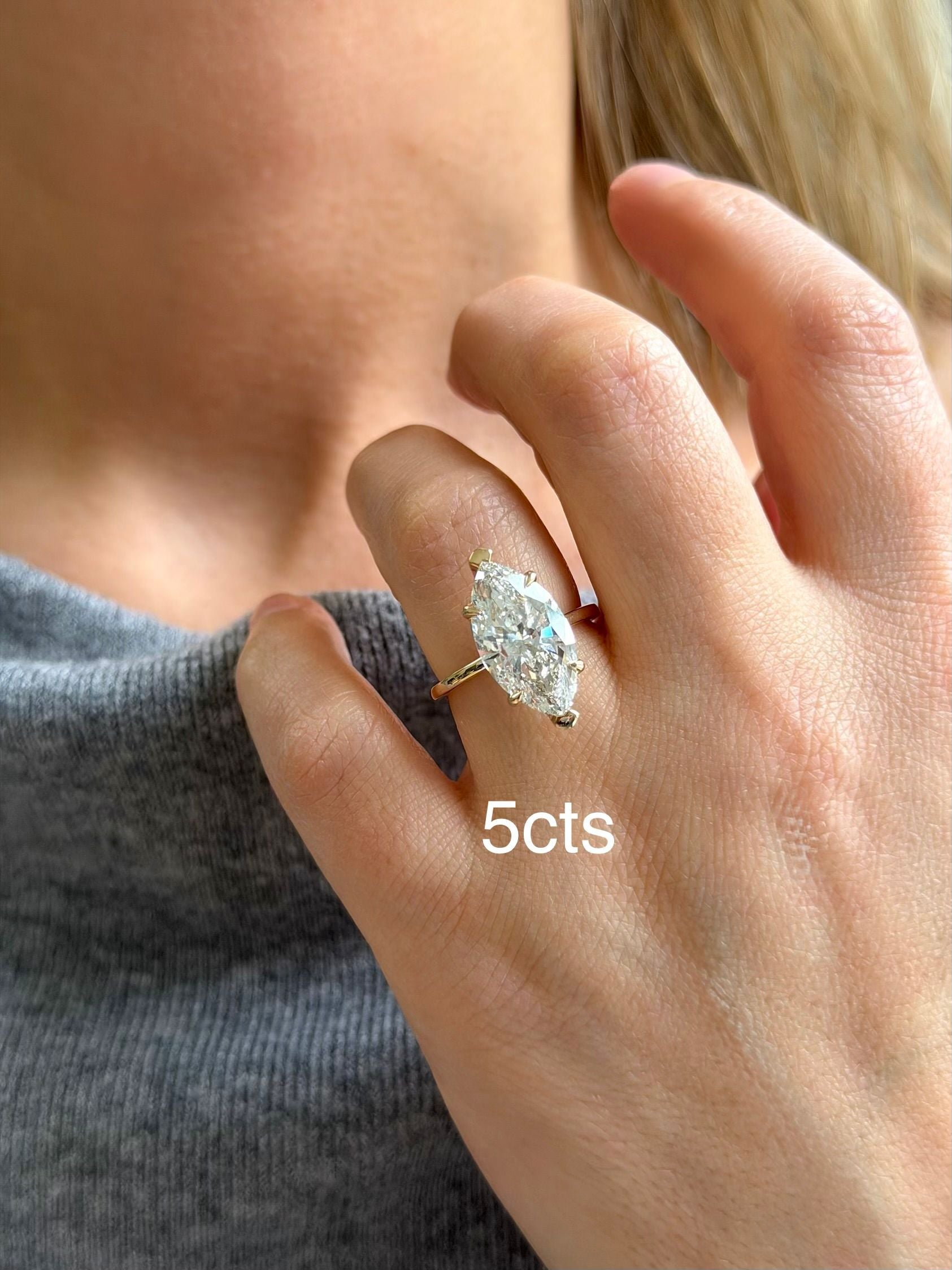 Hand wearing a diamond ring with '5cts' text on a blurred background