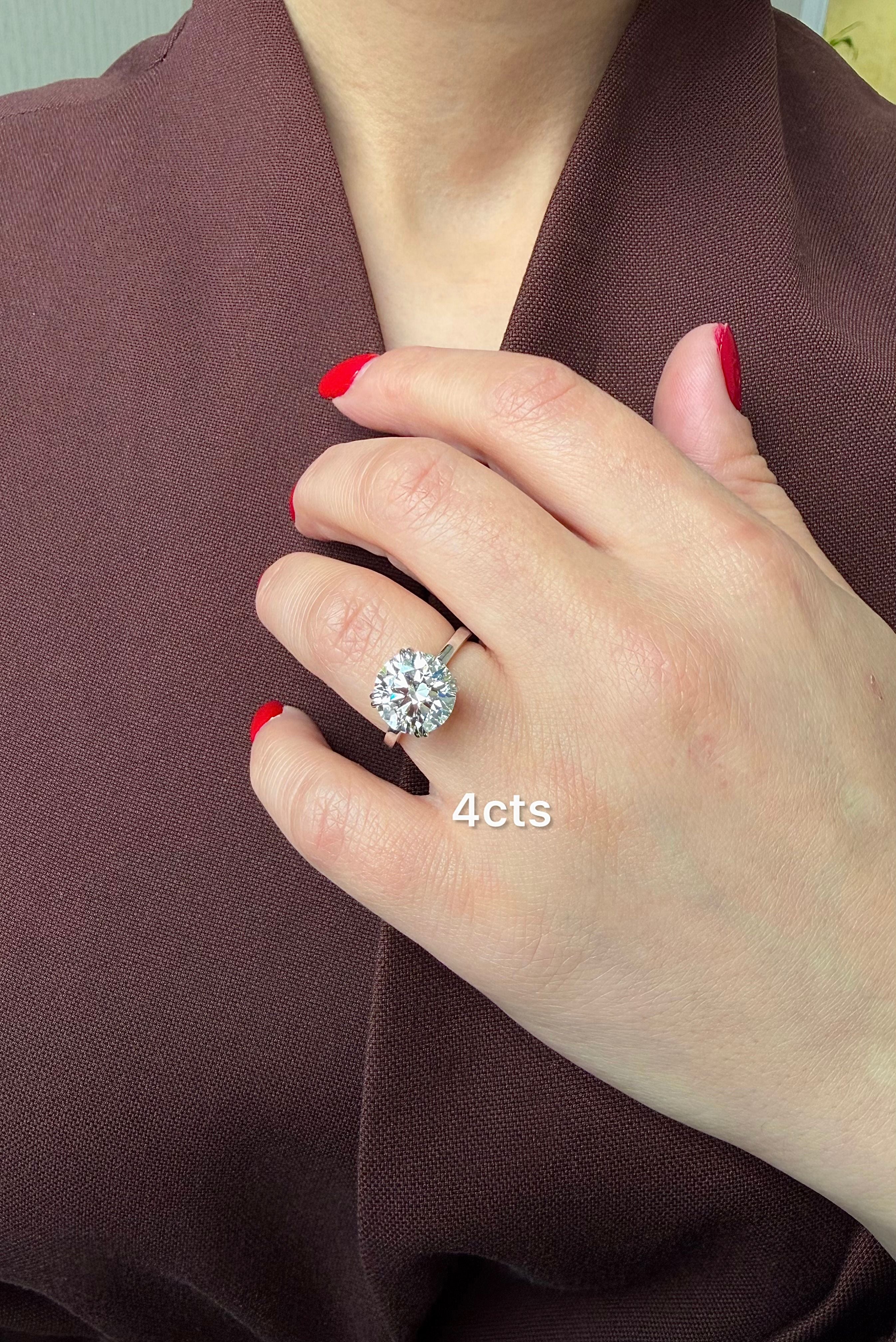 Hand wearing a diamond ring with '4 cts' text, against a brown fabric background