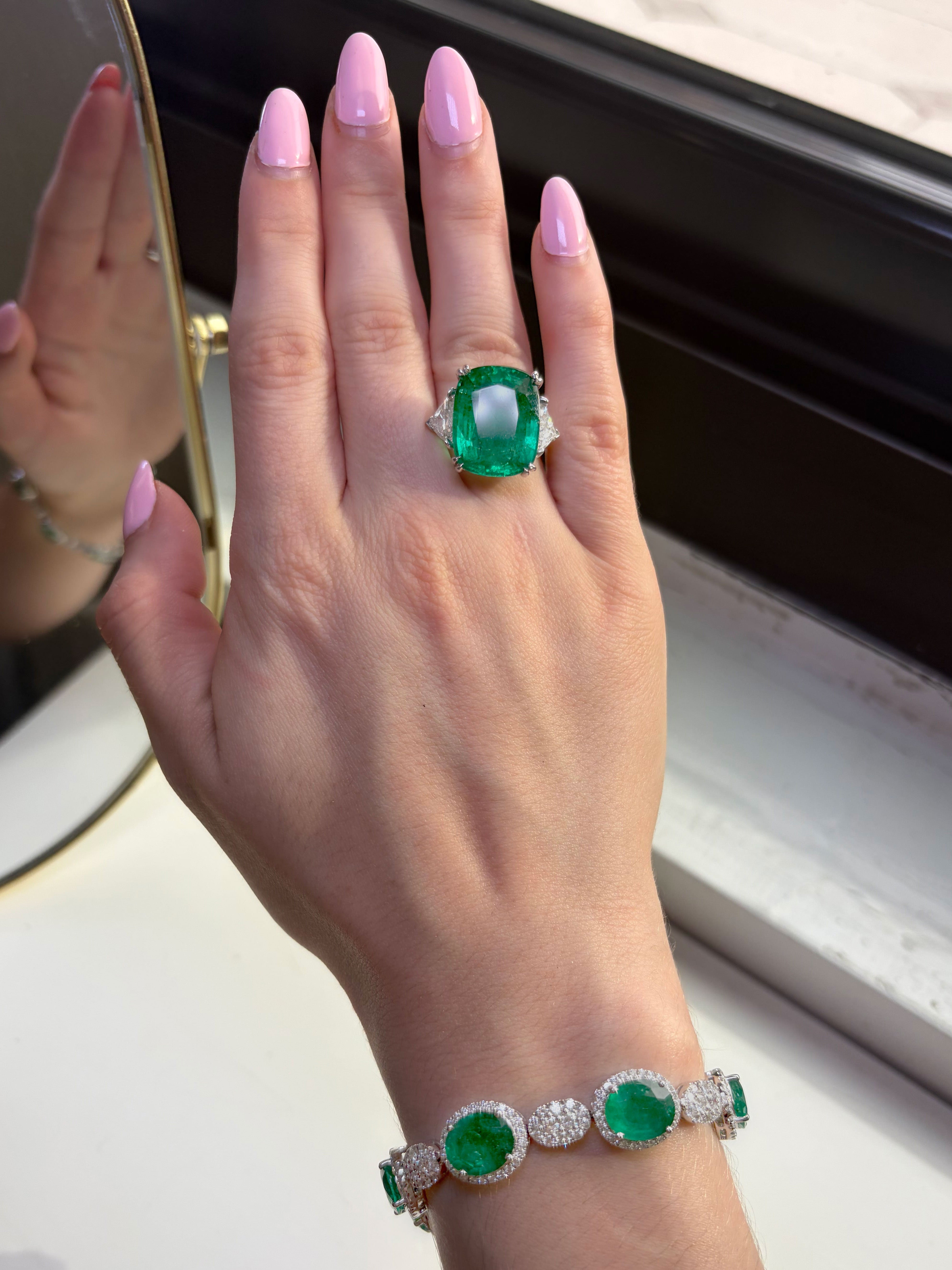 Hand wearing a green gemstone ring with a matching bracelet, against a neutral background.