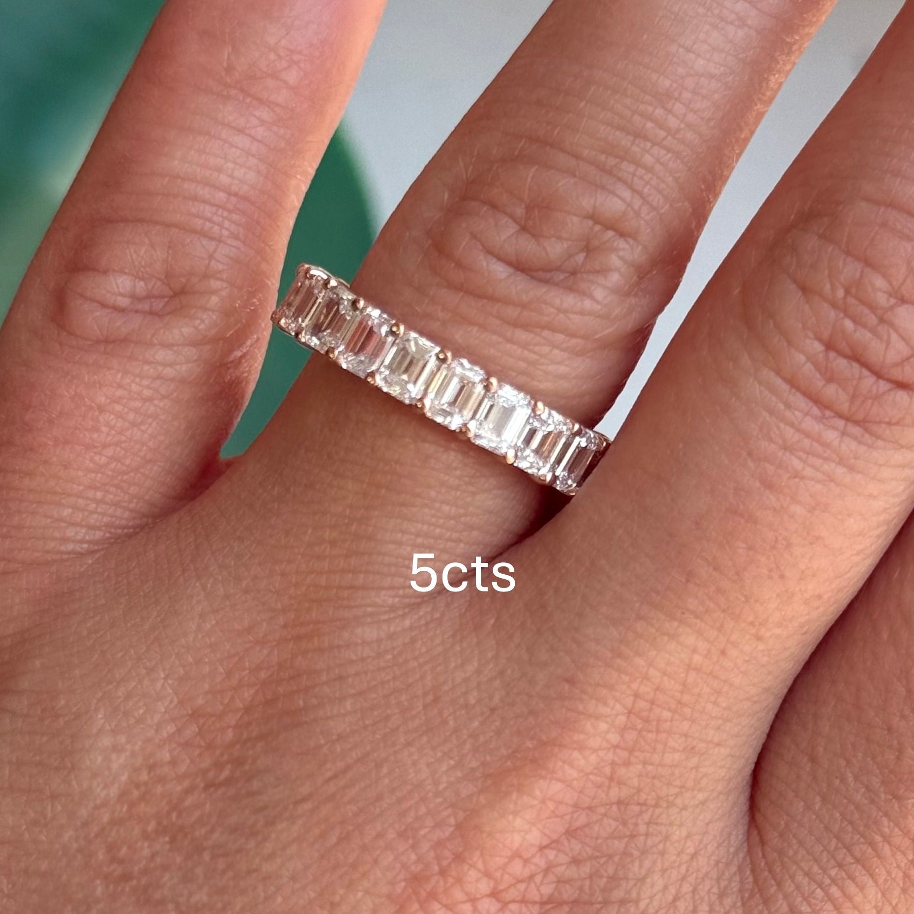 Diamond ring on a finger with '5cts' label against a blurred green background