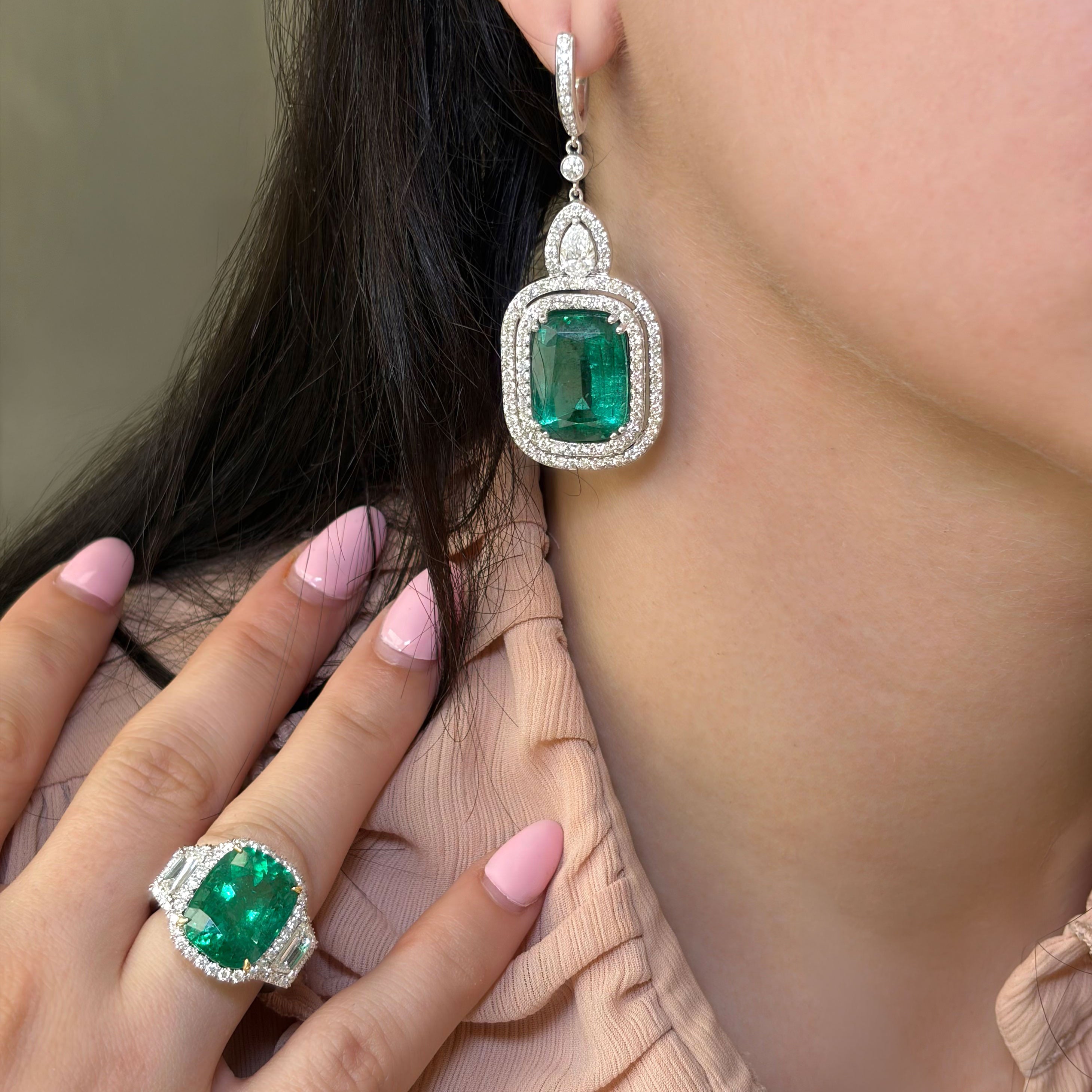 Close-up of a woman wearing emerald green earrings and ring, with a neutral background.