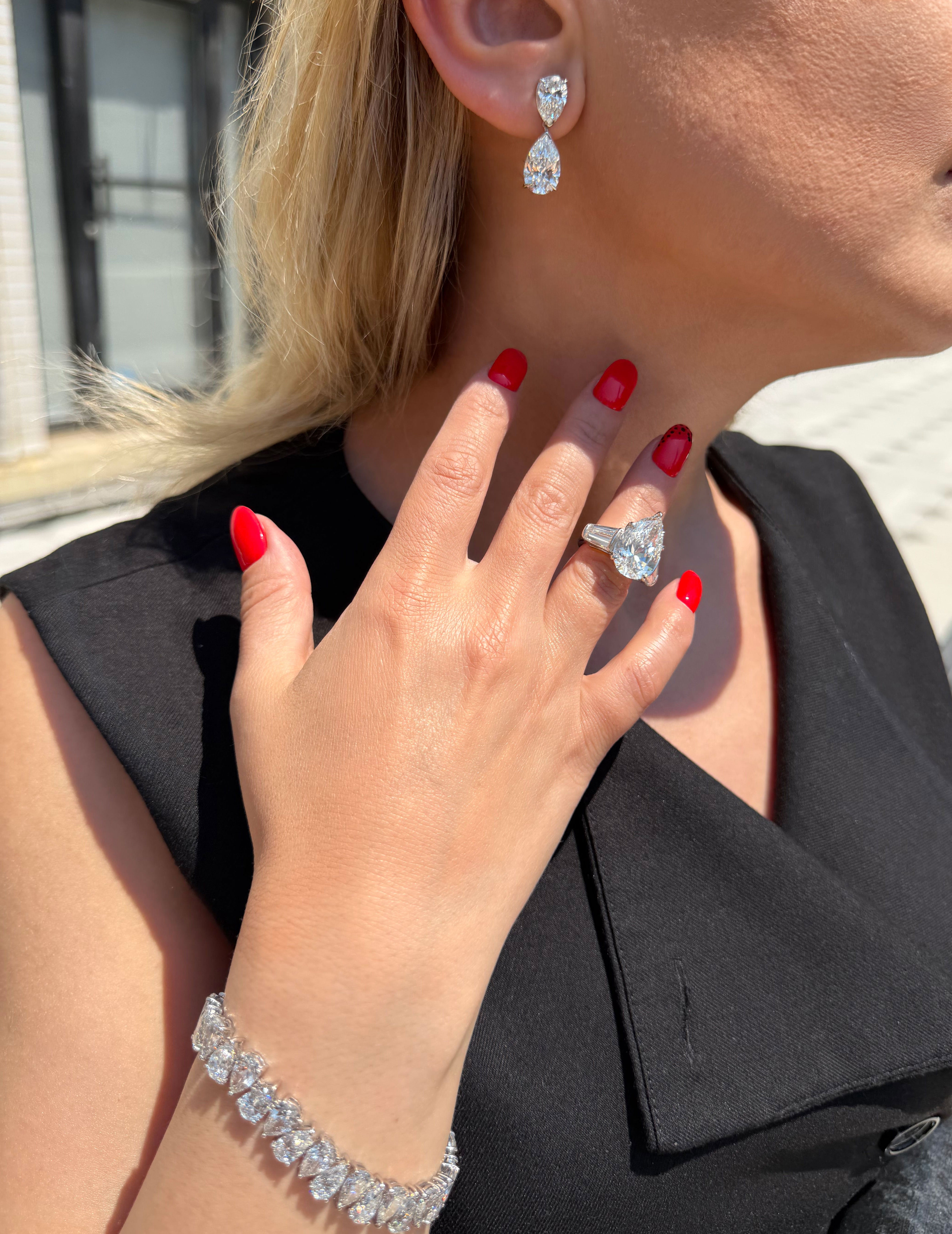 Close-up of a person wearing diamond earrings, ring, and bracelet with a blurred background.