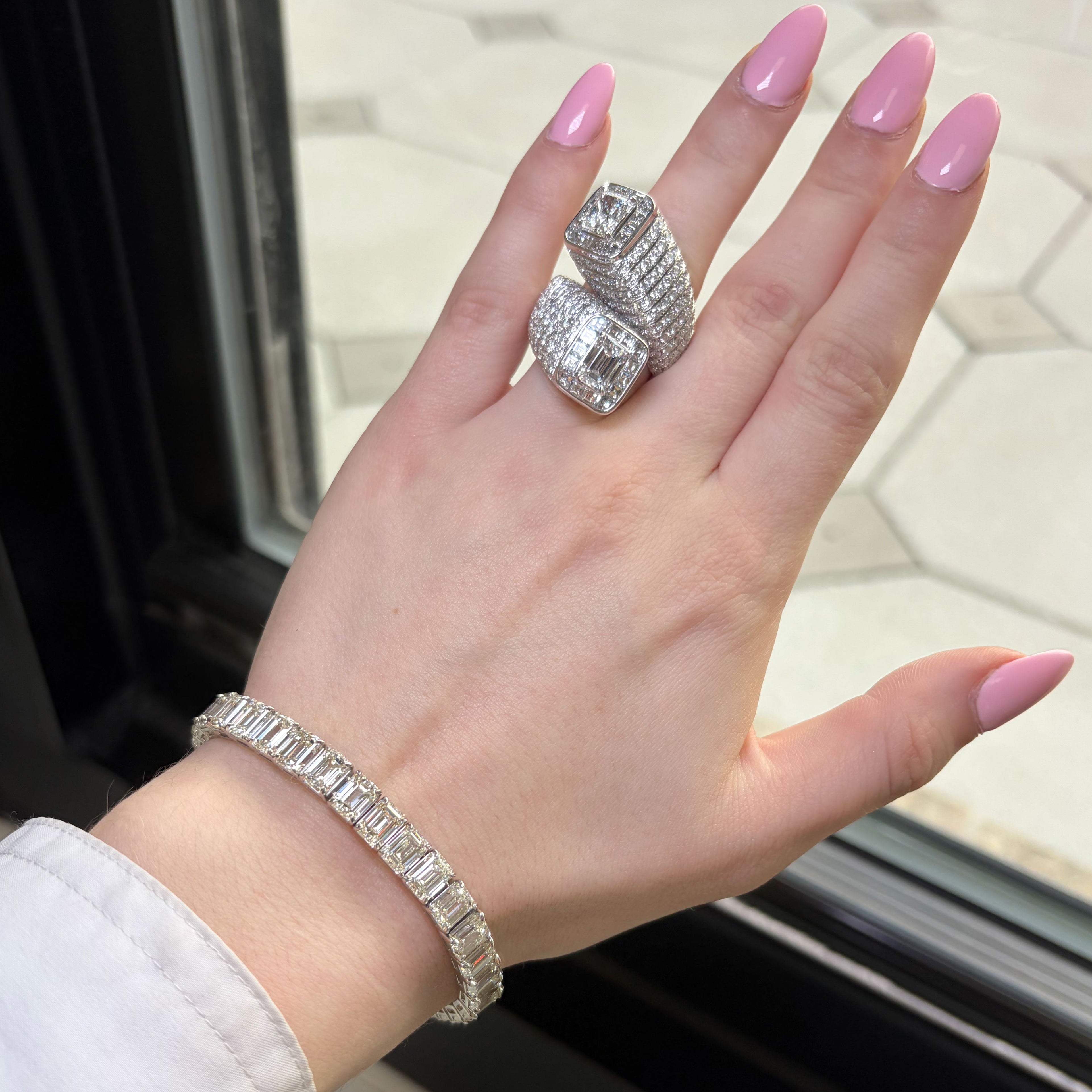 Hand wearing a silver ring and bracelet with pink nail polish, against a neutral background.