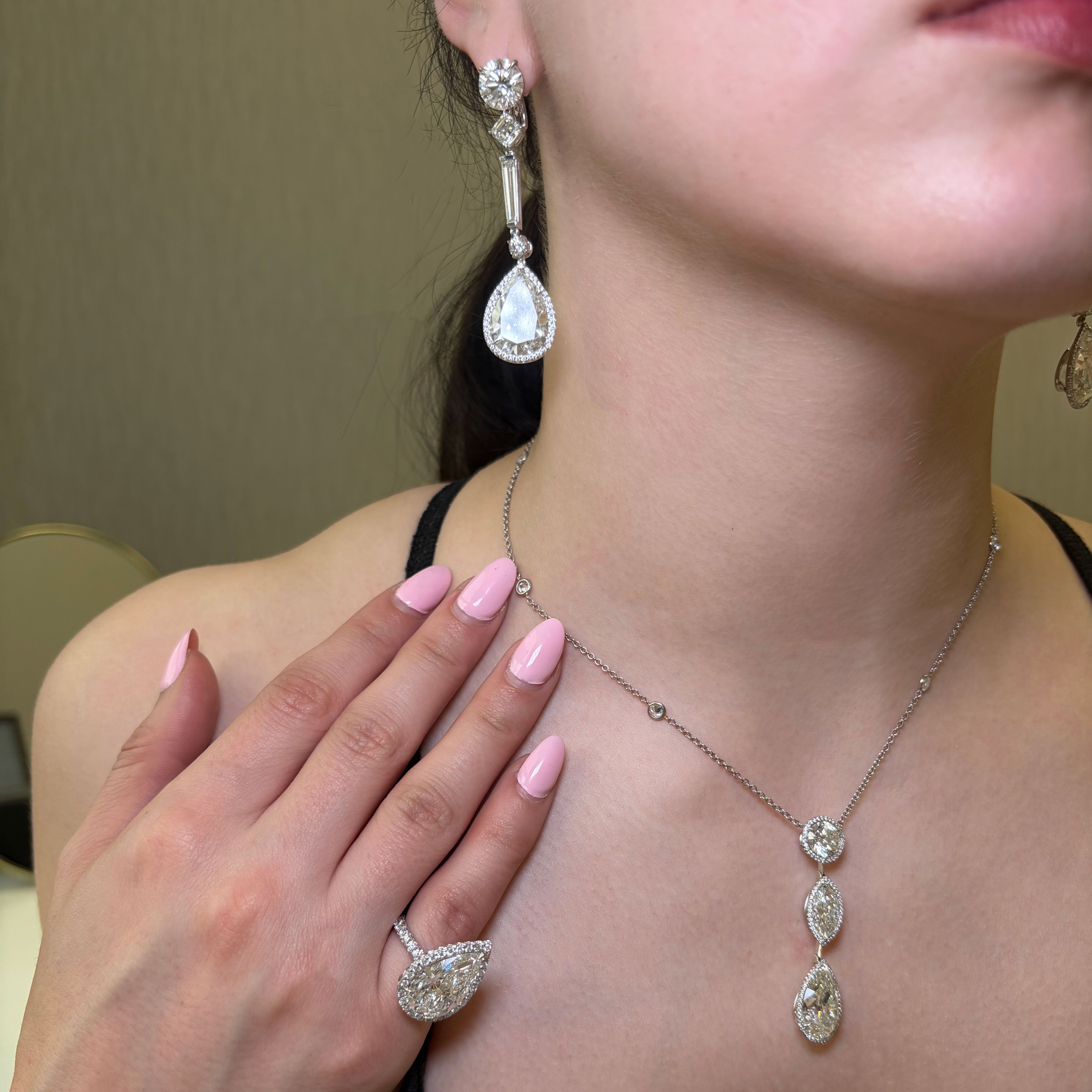 Close-up of a woman wearing a diamond necklace, earrings, and ring with a neutral background.