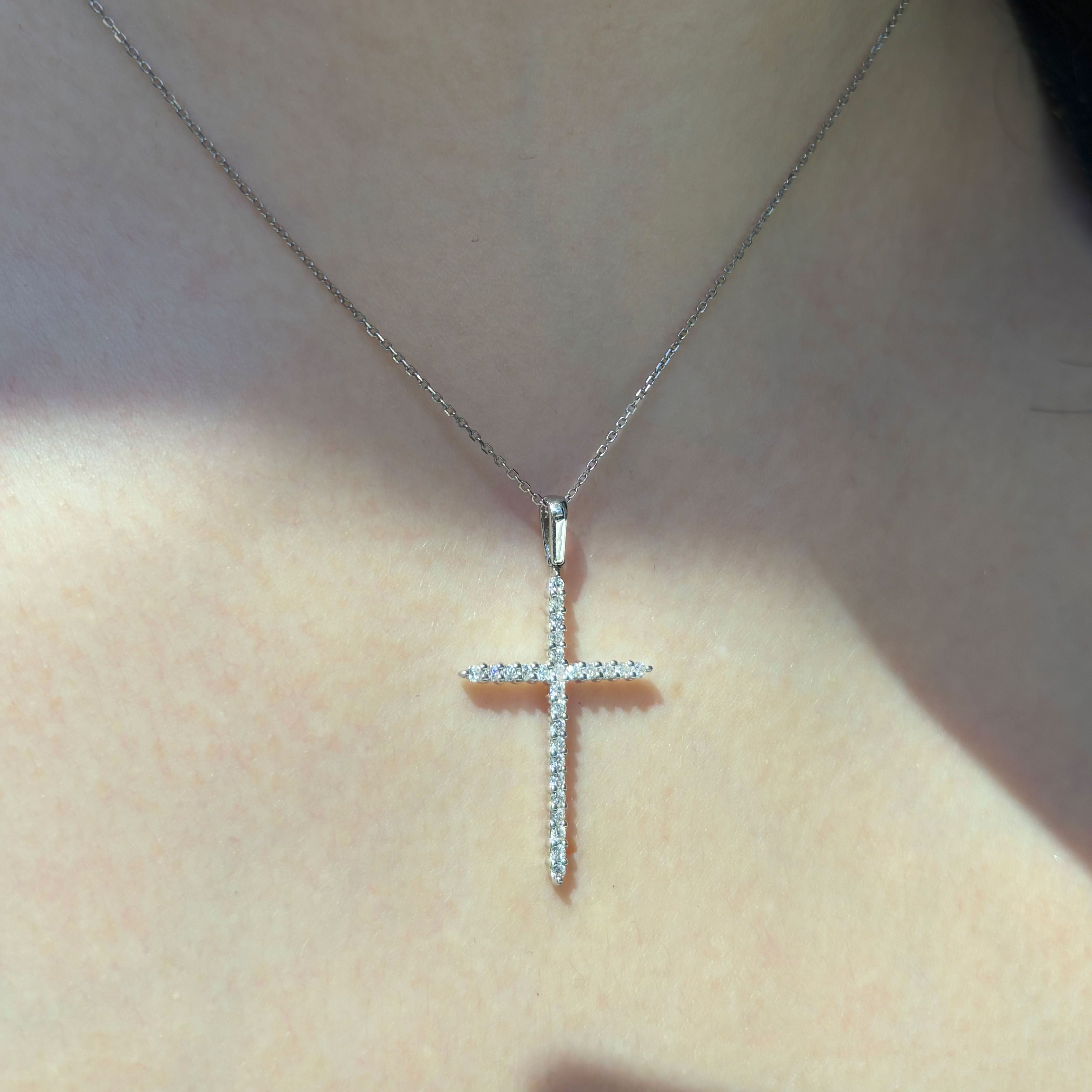 Petite diamond cross pendant worn at the neckline in 14k white gold for scale and proportion