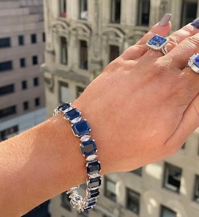 Hand wearing a blue gemstone bracelet and ring with a cityscape background