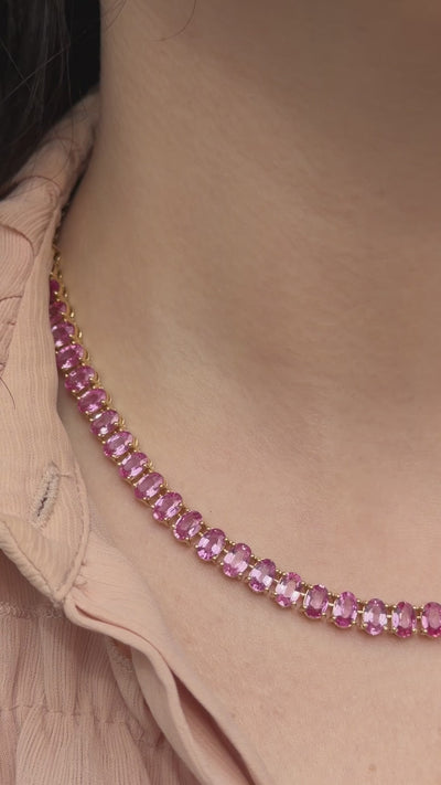 Editorial video of an 18k yellow gold tennis necklace set with 27 carats of oval pink sapphires in a halfway-around design