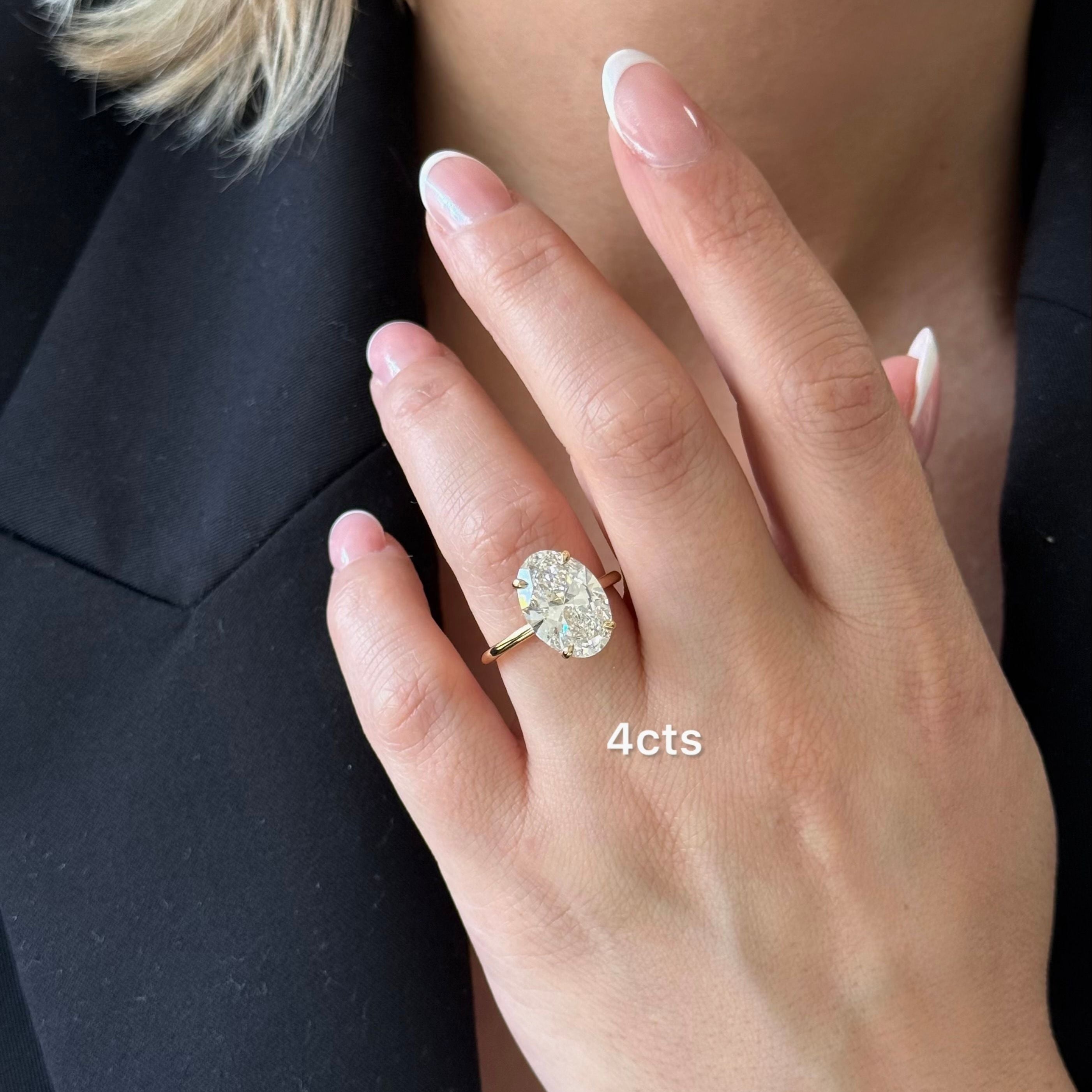 Close-up of a hand wearing a diamond ring with '4 cts' text, against a neutral background.