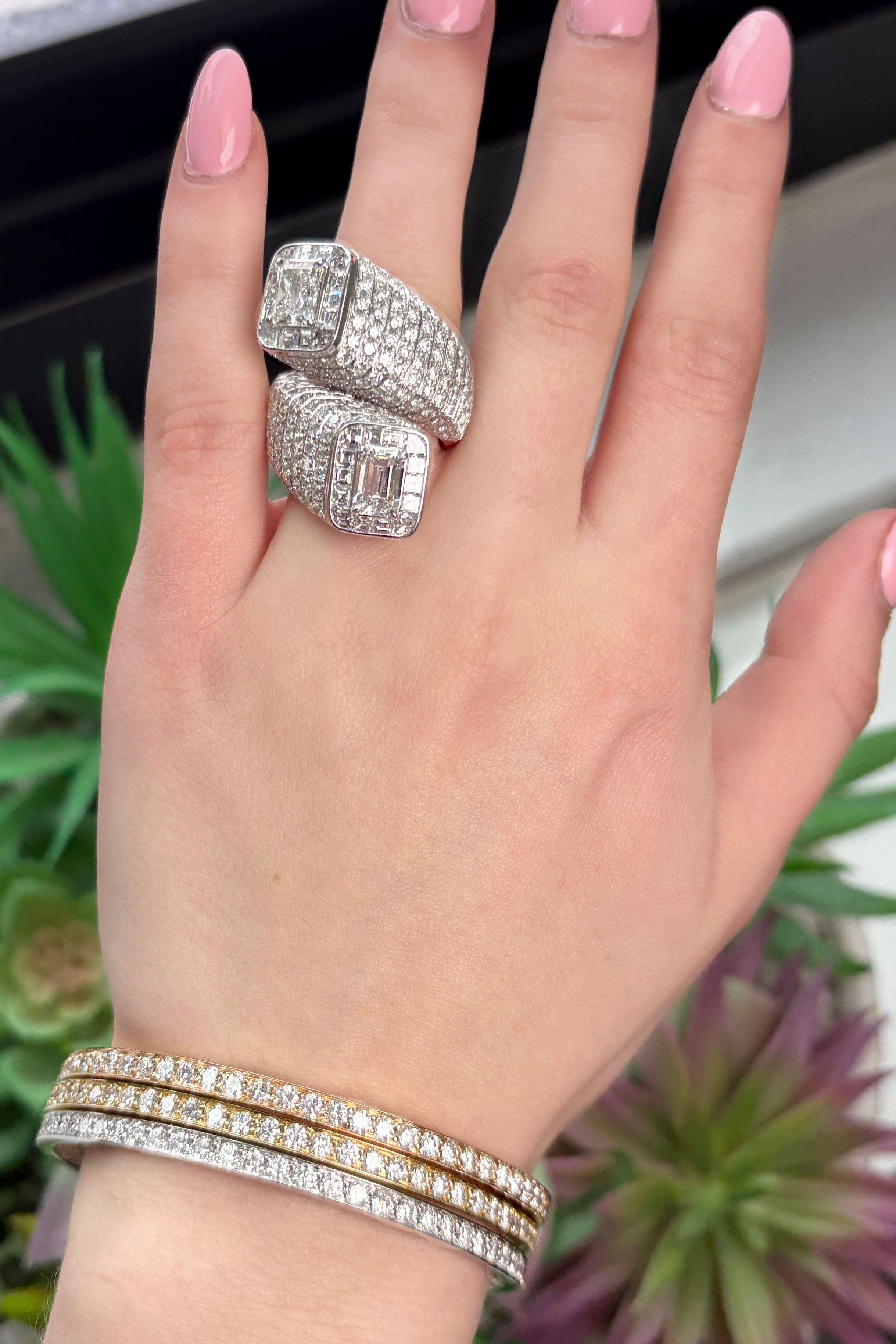 Hand wearing two silver rings with pink nail polish against a blurred plant background
