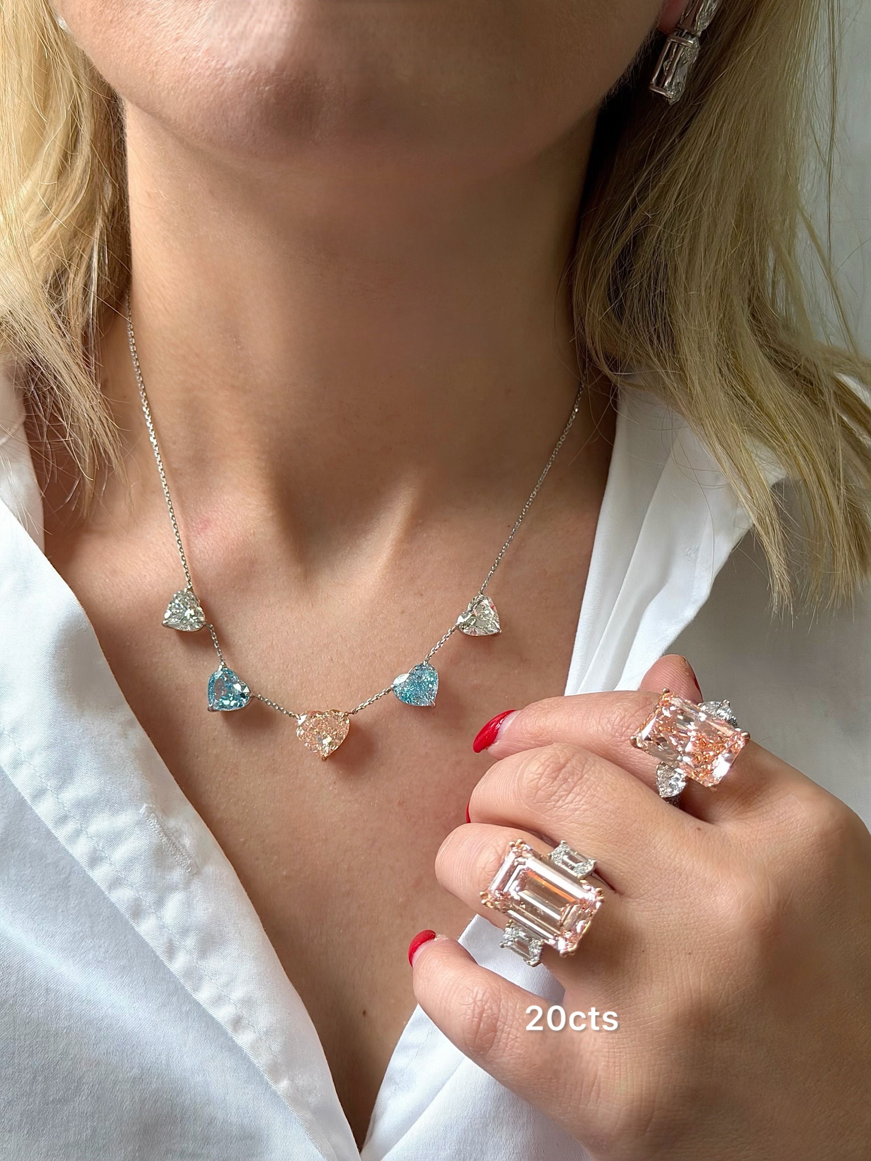 Person wearing a necklace with heart-shaped gemstones and holding a ring with '20cts' text.